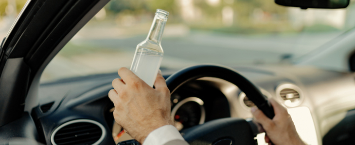 Man driving with alcohol bottle in hand.