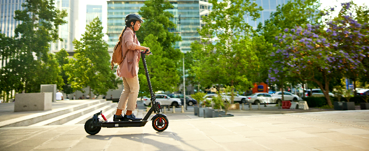 Lady riding an electric scooter in a general area with a helmet on