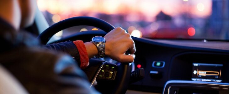 photo of male driver behind the wheel taken from the backseat of the car