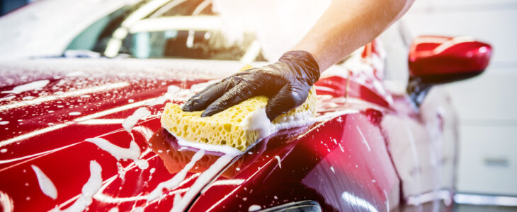 Worker washing red car with sponge on a car wash.